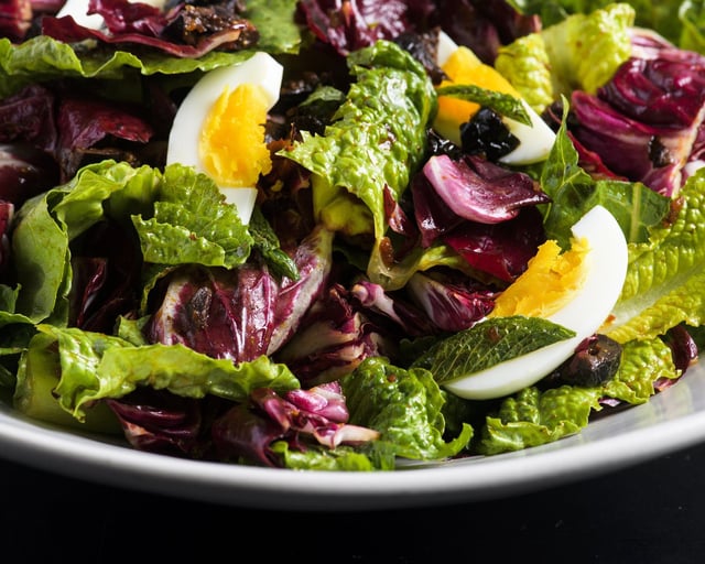This image released by Milk Street shows a recipe for romaine and radicchio salad with olives, eggs and pomegranate vinaigrette. (Milk Street via AP)
