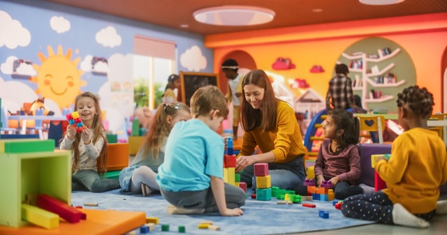 A stock image shows children playing with a teacher in a classroom. This week, deals and discounts are available for teachers across the nation for Teacher Appreciation Week.