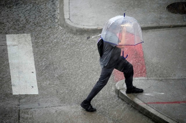 A pedestrian under an umbrella jumps over a water puddle at the corner of Wazeee Street and 20th Avenue as heavy rain packing high winds and large hail sweeps over downtown Denver on Thursday, June 29, 2023. (AP Photo/David Zalubowski)