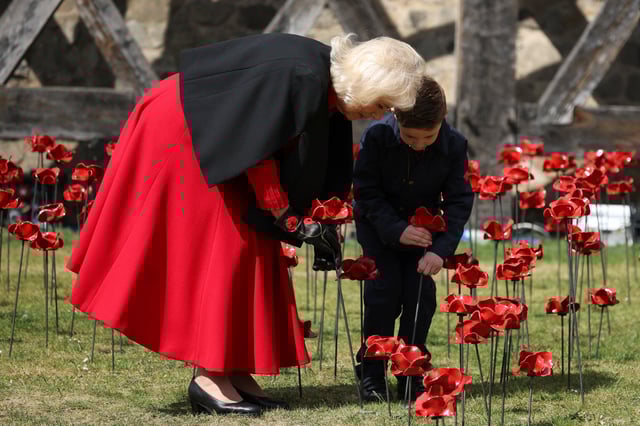 Britain's Queen Camilla holds a ceramic poppy next to Harrison Machin as she visits an installation of 30,000 ceramic poppies, taken from the artwork 'Blood Swept Lands and Seas of Red' (2014), at Tower of London, commemorating the 80th anniversary of Victory in Europe (VE) Day in London, Britain, May 6, 2025. REUTERS/Phil Noble