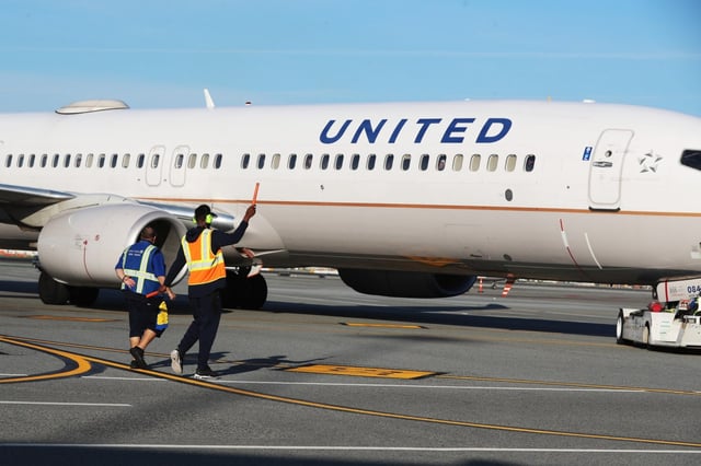 SAN FRANCISCO, CA – FEBRUARY 19: Golden State Warriors forward Andrew Wiggins, right, directs the pilot  with orange glow sticks as teammate guard Damion Lee pushes back a United Airlines aircraft for departure with guidance by employees from the San Francisco Airport in San Francisco, Calif., on Wednesday, Feb. 18, 2020. Wiggins and Lee traded job duties with United employees, made announcements before and after boarding their flight, handout Warriors towels and helped the plane pushed back for departure. Also, passengers and employees took photos with the players. (Ray Chavez/Bay Area News Group)