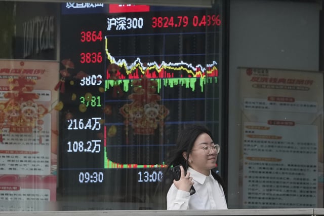 A woman passes by a stock index at a brokerage in Beijing, Wednesday, May 7, 2025. (AP Photo/Ng Han Guan)