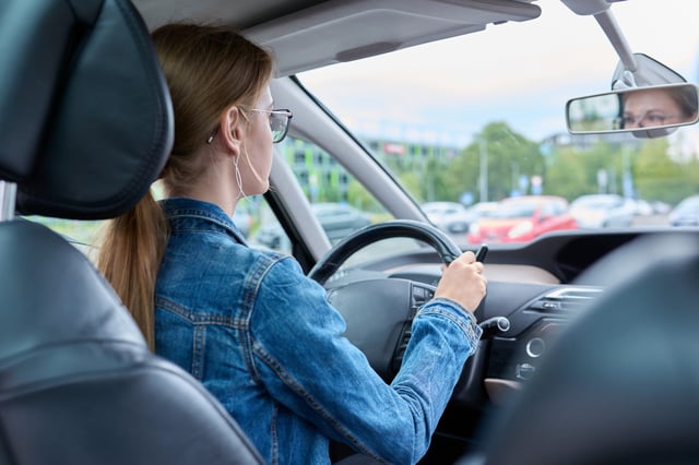 Teenage girl driver in glasses sitting behind wheel of car.