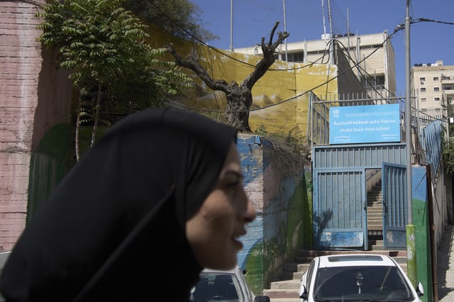 A woman passes the front entrance to the UNRWA Boys' School run by the U.N. agency for Palestinian refugees in the Shuafat Refugee Camp in east Jerusalem, Tuesday, April 29, 2025. (AP Photo/Maya Alleruzzo)