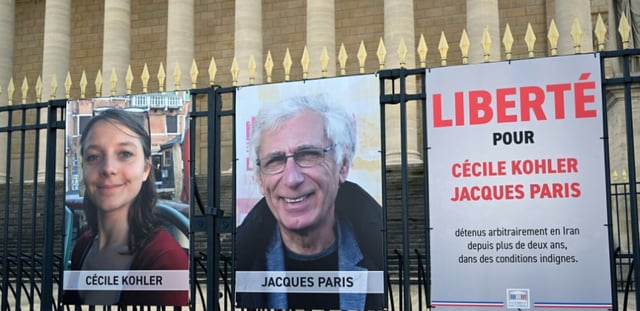 AFP - Des portraits exposés de Française Cécile Kohler (G) actuellement emprisonnée en Iran avec son partenaire, le Français Jacques Paris (C) devant le Palais Bourbon, l'Assemblée nationale française à Paris, le 25 mars 2025