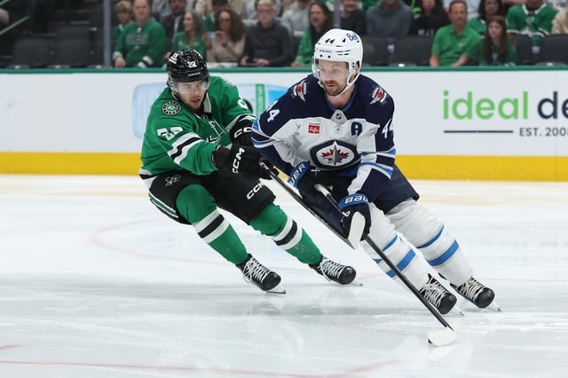 Josh Morrissey #44 of the Winnipeg Jets skates with the puck in front of Mavrik Bourque #22 of the Dallas Stars during the first period at American Airlines Center on April 10, 2025 in Dallas, Texas.