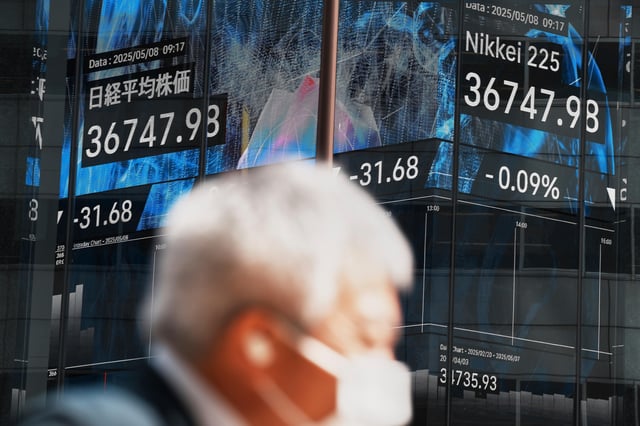 A person walks in front of an electronic stock board showing Japan's Nikkei index at a securities firm Thursday, May 8, 2025, in Tokyo. (AP Photo/Eugene Hoshiko)