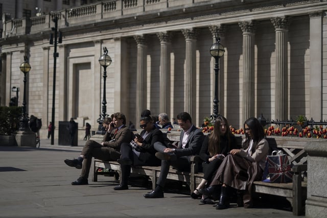 People sit on the benches outside the Bank of England in the financial district known as The City, in London, Wednesday, April 9, 2025. (AP Photo/Alberto Pezzali)
