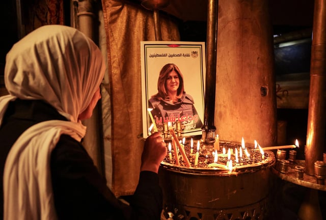 A woman lights a candle in front of a poster depicting veteran Al-Jazeera journalist Shireen Abu Akleh, who was shot dead while covering an Israeli army raid in Jenin, at the the Church of the Nativity in the West Bank biblical city of Bethlehem on May 11, 2022.