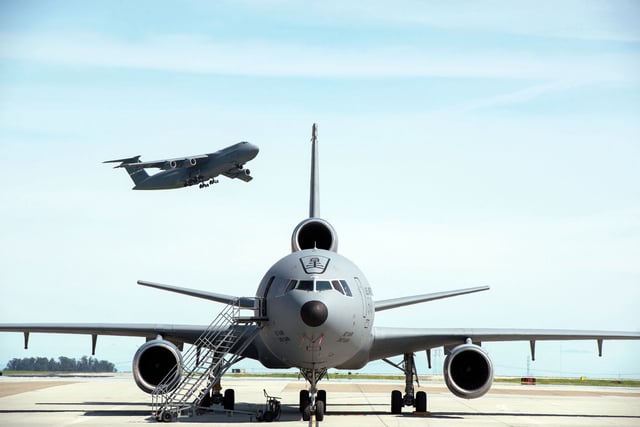 A KC-10 Extender is parked on the ramp as a C-5M Super Galaxy takes off at Travis Air Force Base in 2017.