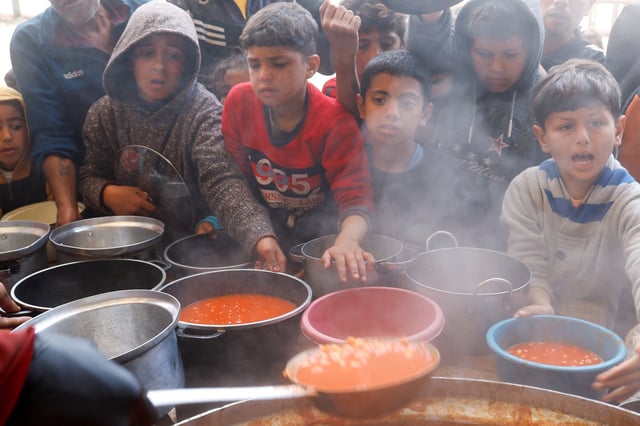 Palestinian children wait to receive food cooked by a charity kitchen, during the Muslim holy month of Ramadan, in Khan Younis, in the southern Gaza Strip, March 9, 2025. REUTERS/Hatem Khaled/File Photo