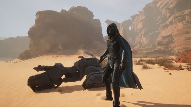 A Dune: Awakening character standing in front of their bike, surrounded by mostly desert and mountainous terrain. 