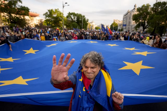 A man with Romanian and European Union flags draped over his shoulders waves in front of a large EU flag, during a pro-EU rally ahead of the second round of the presidential election redo in Bucharest, Romania, Friday, May 9, 2025. (AP Photo/Andreea Alexandru)