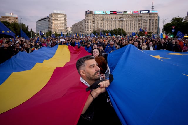 Demonstrators hold large Romanian and European Union flags during a pro-EU rally ahead of the second round of the presidential election redo in Bucharest, Romania, Friday, May 9, 2025. (AP Photo/Andreea Alexandru)