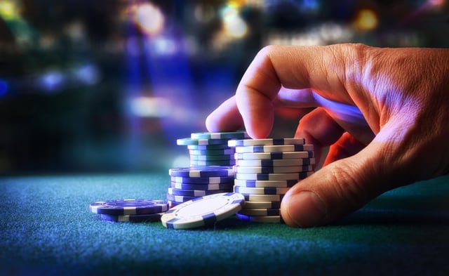 Hand betting game chips on felt mat with game room in the background. Front view.