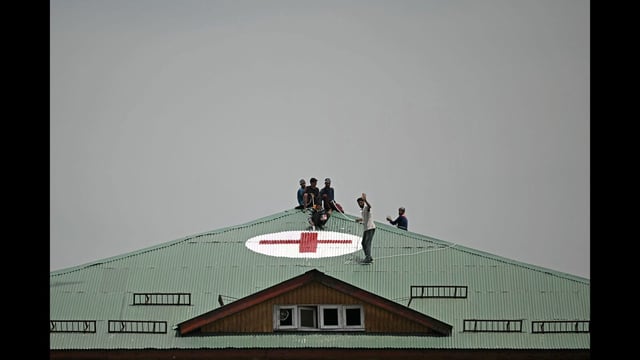 Workers paint a red cross symbol over the roof of a hospital in Srinagar amid tension along the border. (AFP)