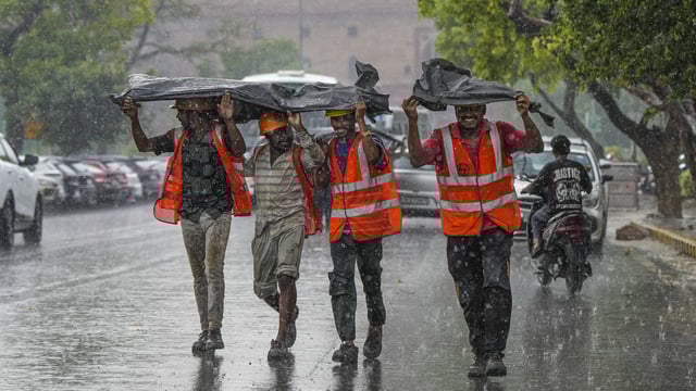 Workers huddle together under a plastic sheet during rainfall, in New Delhi.