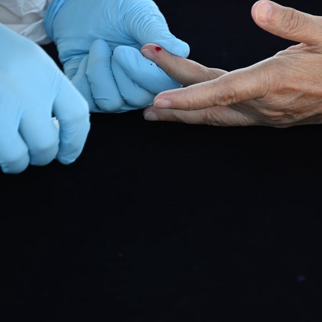 gloved hands pricking a finger for blood