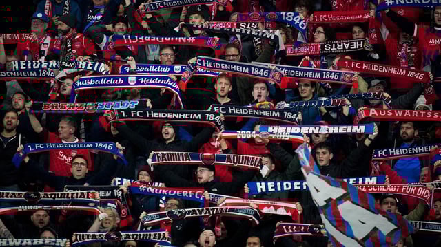 Fans des 1. FC Heidenheim halten im Stadion Schals in die Höhe.