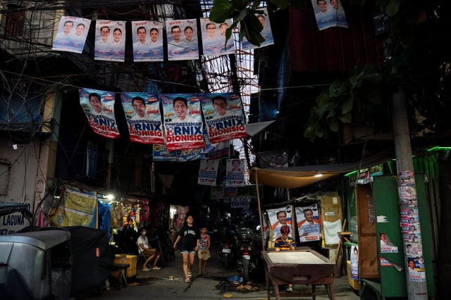 People walk past a street with campaign posters put up, a day before the May 12 midterm elections, in Manila, Philippines, May 11, 2025. REUTERS/Lisa Marie David
