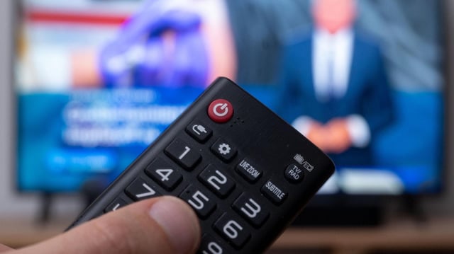 Eine Hand hält eine Fernbedienung für ein Fernseher.