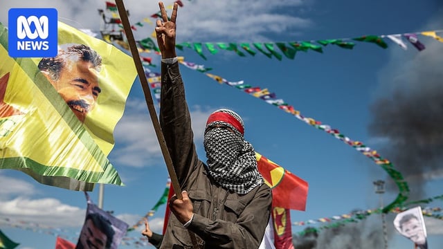A Kurdish man wearing a mask flashes the v-sign as he holds up a flag with a picture of the jailed PKK leader Abdullah Ocalan