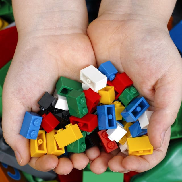 Lego Bricks in child's hands with Lego Duplo blocks and toys background