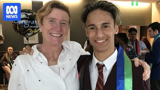 A woman standing next to a teen boy at his school graduation