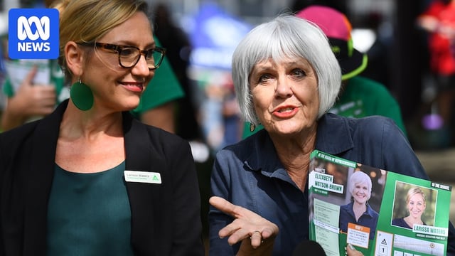 two women, one holding a greens pamphlet, talk to media