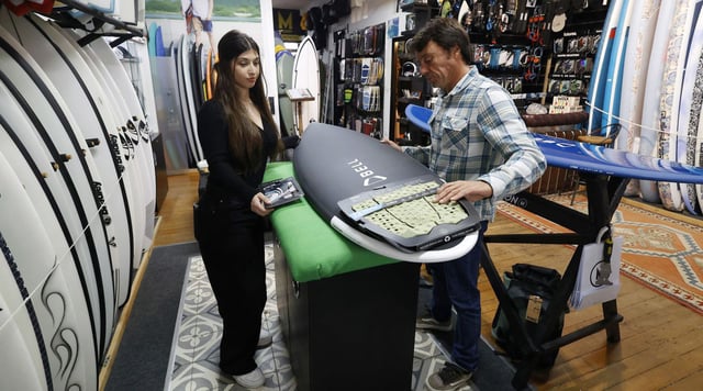 Miguel preparando con ayuda una tabla de surf en Mission, donde se preparan para el subidón del verano.