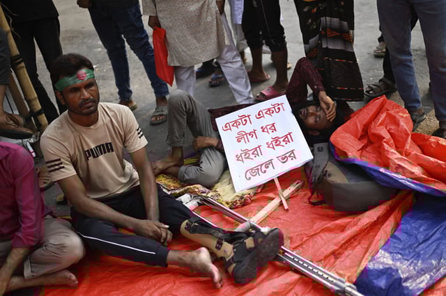 Protesters, who were injured in protests against former Prime Minister Sheikh Hasina last year, sit with a banner that reads 'One by one Awami League supporters should be detained and taken into custody' during a protest, in Dhaka, Bangladesh, Sunday, May 11, 2025. (AP Photo/Mahmud Hossain Opu)