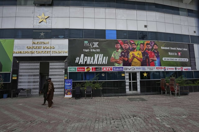 Workers walk past an advertisement board of Pakistan Super League Twenty20 tournament with the pictures of cricketers, installed at the Rawalpindi Cricket Stadium, in Rawalpindi, Pakistan, Friday, May 9, 2025. (AP Photo/Anjum Naveed)