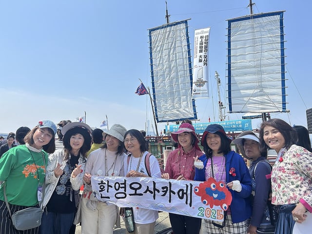 Japanese citizens participating in a ceremony to celebrate the arrival of a replica ship of the past Joseon Tongsinsa diplomatic mission from Korea pose for a photo with a banner welcoming the ship at the Port of Osaka in Japan on May 13, 2025. (Yonhap)