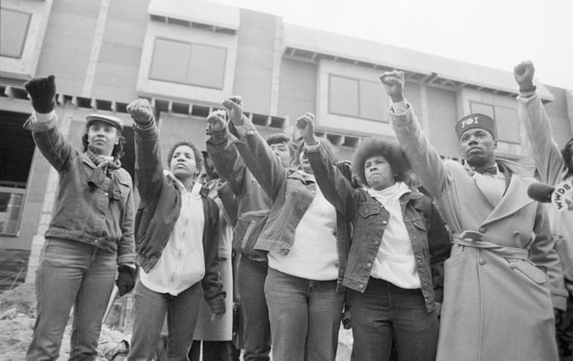 Mourners of MOVE members killed in the bombing by the Philadelphia Police stand in front of their former headquarters as the funeral procession for John Africa passes.