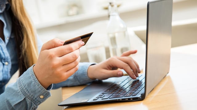 Eine Frau sitzt mit Kreditkarte vor einem Laptop.