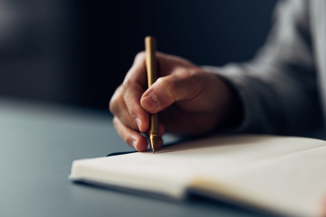 An individual meticulously jotting down notes in a notebook using an elegant pen, with a close-up on the writing hand.