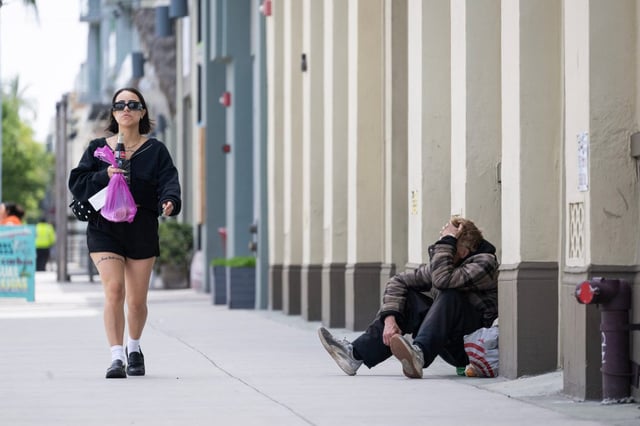 A woman walks past a homeless man on West 3rd St. in downtown Long Beach on Monday, May 12, 2025. Governor Gavin Newsom is urging California’s local governments to begin clearing homeless encampments, escalating the state’s efforts to ban makeshift camps on sidewalks and in parks. (Photo by Drew A. Kelley, Press-Telegram/SCNG)