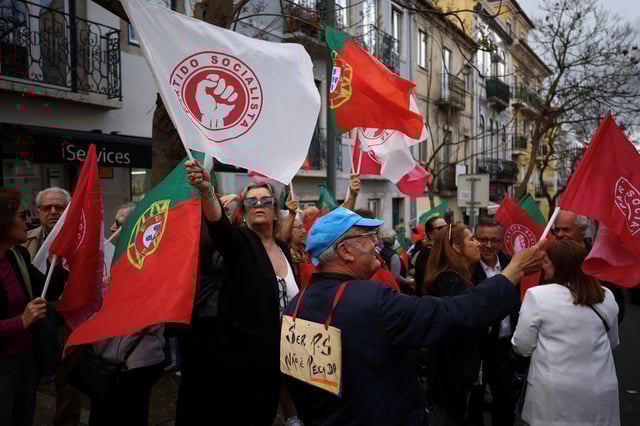 People wave flags of the Socialist party (PS) as a man wears a card reading, "To be socialist is not a sin", while waiting for PS leader Pedro Nunes Santos, for a rally ahead of the snap elections, in Lisbon, Portugal, May 13, 2025. REUTERS/Pedro Nunes