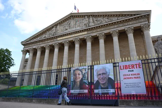 A woman walks past posters with the portraits of Cecile Kohler and Jacques Paris, two French citizens held in Iran, on the day of support rallies to mark their three-year detention and to demand their release, in front of the National Assembly in Paris, France, May 7, 2025. The slogan reads "Freedom for Cecile Kohler and Jacques Paris". REUTERS/Abdul Saboor
