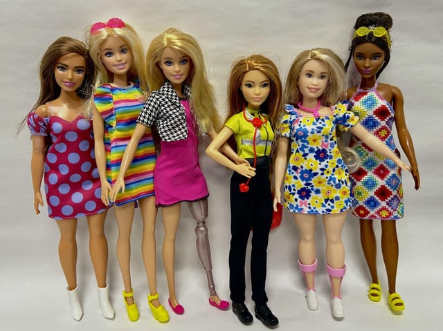 The Barbie Team (from left to right): Barbie Fashionista (#171) wears a high heel white ankle boot, Barbie Fashionista (#197) wears an amazing yellow platform heel with ankle straps, Barbie Interior Designer wears ballet flats on both her foot and prosthetic limb, Barbie Paramedic has her workboots ready to go, Barbie Fashionista (#208) has Down Syndrome and uses sneakers to accommodate her ankle foot orthoses, and Barbie Fashionista (#210) models comfy yellow slides. (Dredit: Cylie Williams, CC-BY 4.0 (https://creativecommons.org/licenses/by/4.0/))