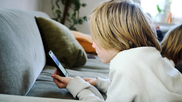 Ein Junge liegt auf einem Sofa und guckt auf sein Smartphone.