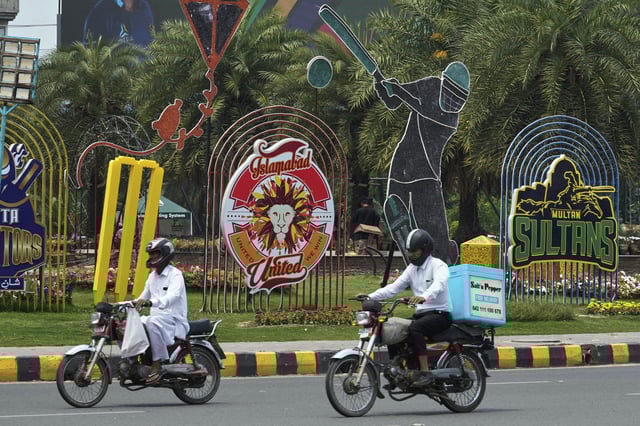 Motorcyclists drive past an advertisement of Pakistan Super League Twenty20 tournament displayed along a roadside in Lahore, Pakistan, Friday, May 9, 2025. (AP Photo/K.M. Chaudary)