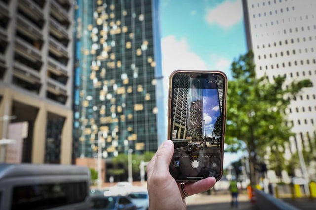 A pedestrian stops to take a photo of the storm-damaged Wells Fargo building in Houston as storm cleanup continued on May 20, 2024. The city closed off streets in a six-block exclusion zone downtown, from McKinney to Polk streets and from Smith to Travis, to ease traffic around the area littered with broken glass and debris.