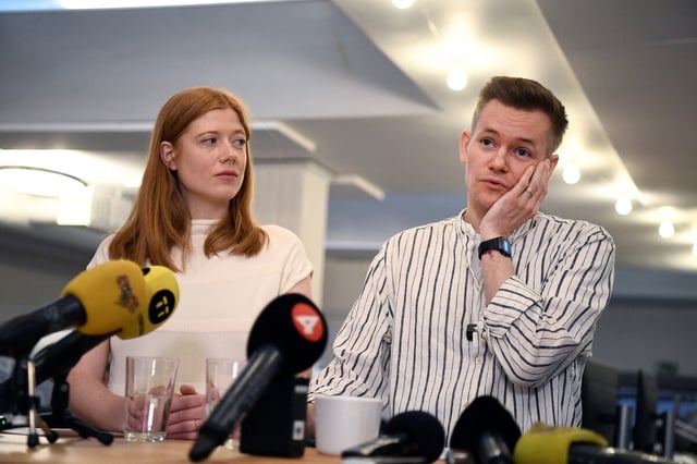 Joakim Medin und seine Frau Sofie Axelsson stehen hinter einem Pult mit Mikrofonen. Joakim hält sich seine rechte Hand an die Wange