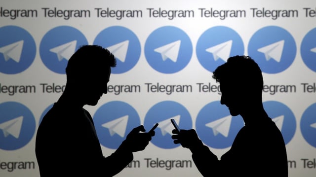 Zwei Mobilfunknutzer vor einer Wand mit Logos des russischen Messengerdienstes Telegram