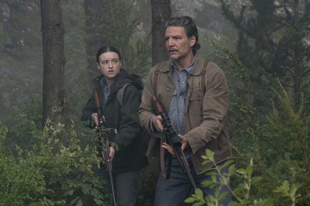Joel (Pedro Pascal) and Ellie (Bella Ramsey) stand on alert in a forest in The Last of Us season 2