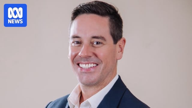 A man wearing a collared shirt and jacket smiles for the camera in a professional headshot.