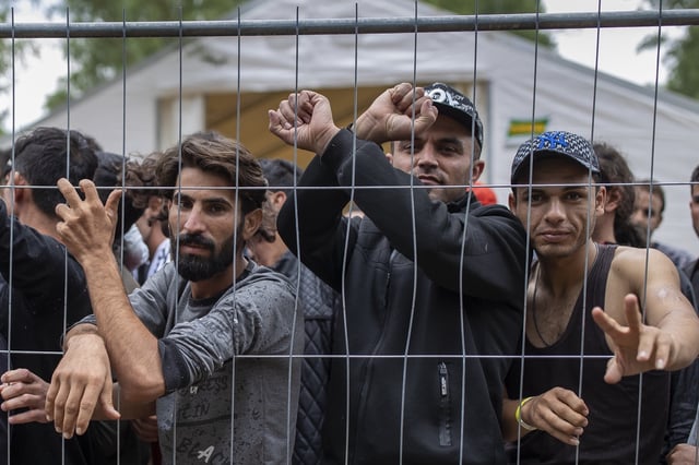 FILE - In this file photo taken on Wednesday, Aug. 4, 2021, Migrants stand behind a fence inside the newly built refugee camp in the Rudninkai military training ground, some 38km (23,6 miles) south from Vilnius, Lithuania. (AP Photo/Mindaugas Kulbis, File)