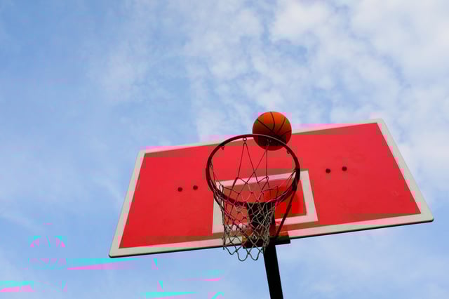 a basketball flies into the basket, against the blue sky, in an open area. Theme of sports, achievement of goals.