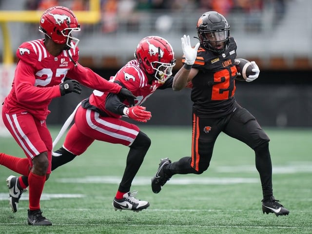  B.C. Lions’ Jason Huntley, right, carries the ball while being pursued by Calgary Stampeders’ Darren Evans, second left, and Godfrey Onyeka during the second half of a preseason CFL football game, in Langford on Monday